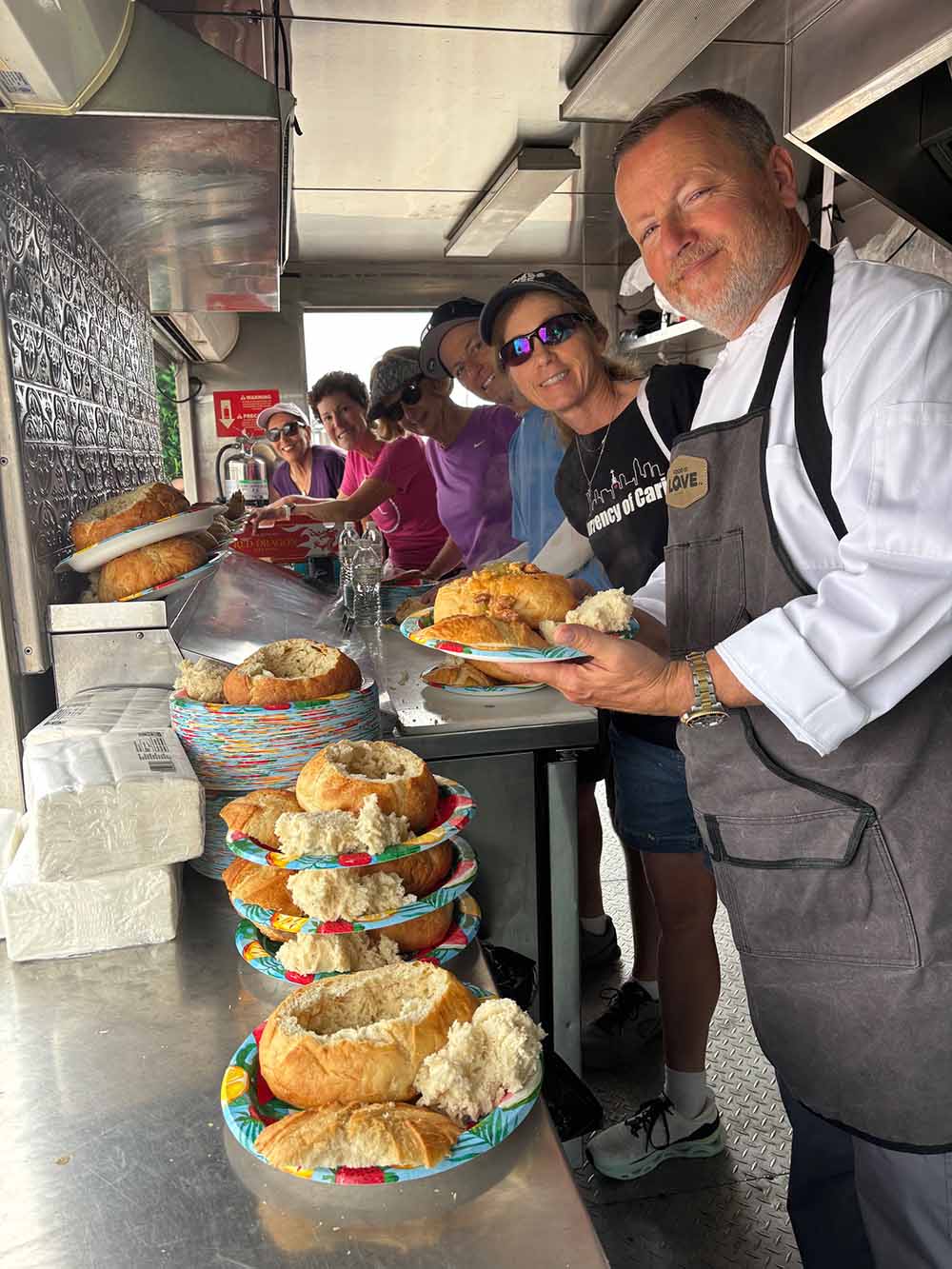 A Soulcial Kitchen chef and smiling volunteers serving bread-bowl meals from a food truck